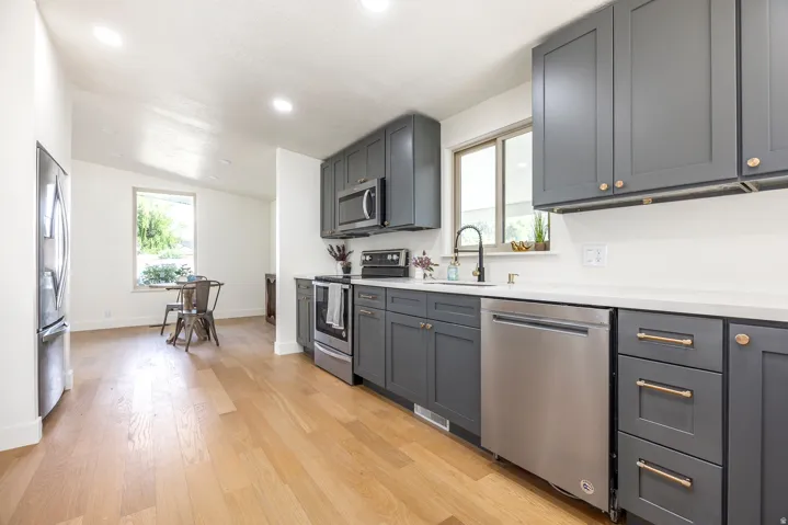 Modern kitchen featuring dark grey cabinetry, stainless steel appliances, light-toned countertops, and wood-finish flooring