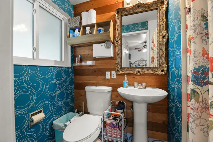 A colorful, character-filled bathroom features a pedestal sink, decorative tile-inspired walls, wood accents, and a framed mirror. Connected to the Primary Bedroom