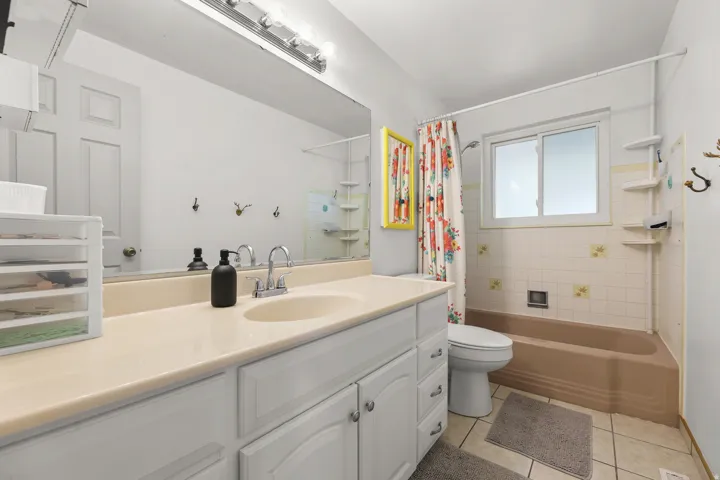 A spacious bathroom features a long vanity with ample storage, tiled flooring, a tub and shower combination, and a bright window for natural light.