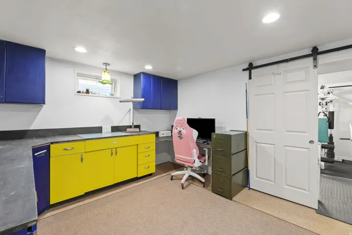 A dedicated workspace features colorful cabinetry, a durable work surface, built-in storage, and direct access to an adjacent room. Featuring recessed lighting and a barn style door to basement bedroom