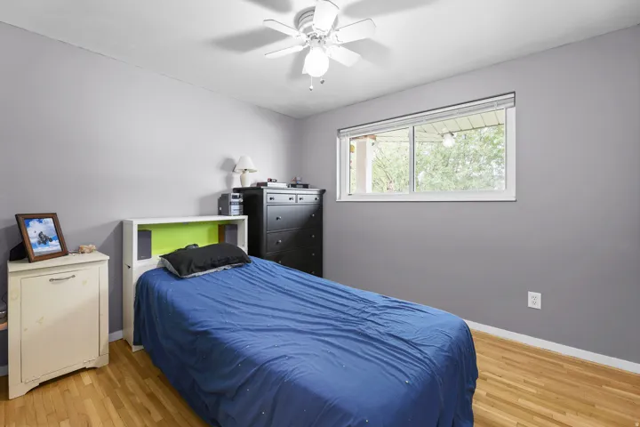 Hardwood flooring, a ceiling fan, and a large window looking out the front of the home create a comfortable retreat.