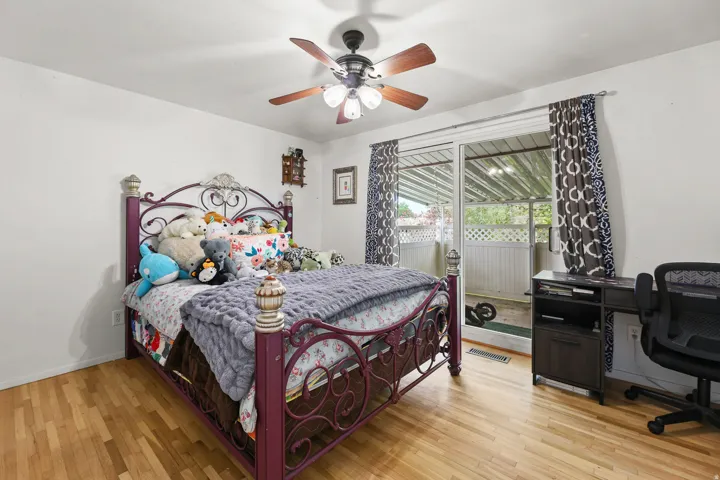 Hardwood floors, a ceiling fan, and a large window overlooking the covered outdoor area provide a comfortable, primary bedoom space.