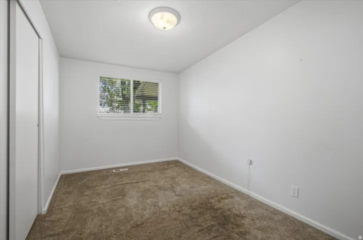 Neutral wall finishes, window with blinds, carpeted flooring, flush mount ceiling light, and bi-fold closet doors