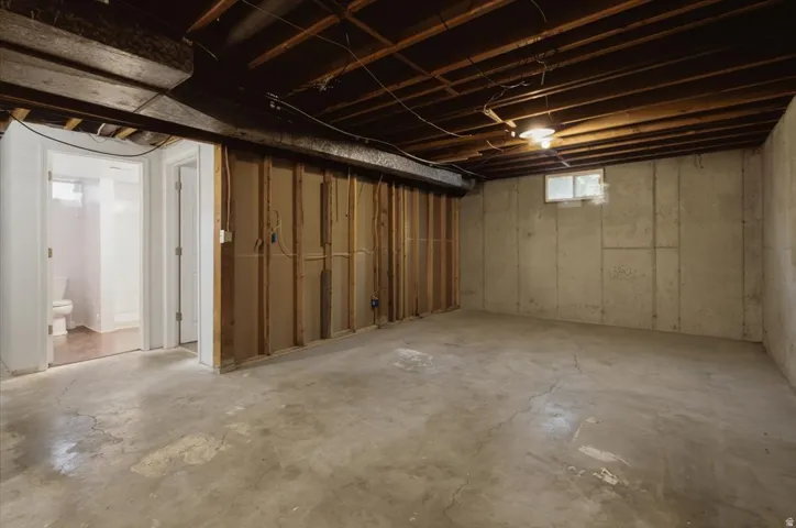 Unfinished basement with exposed ceiling beams, concrete flooring, window well, and framed partition walls