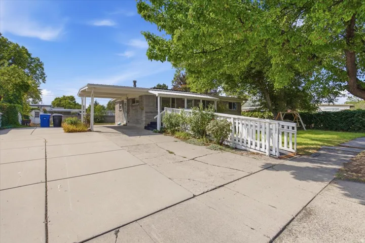 Single-story residence featuring a carport, concrete driveway, and a white picket fence
