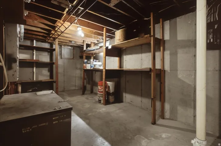 Concrete floor and walls, exposed wood ceiling joists, built-in wooden shelving, and overhead lighting