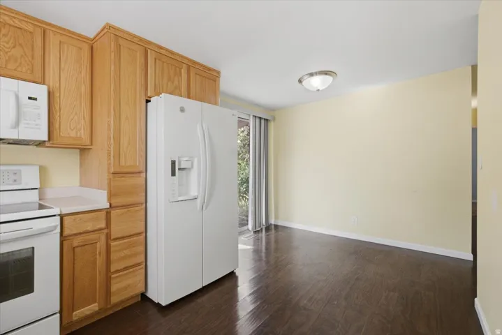 Kitchen with wood cabinetry, white appliances, solid surface countertops, and wood-finish flooring