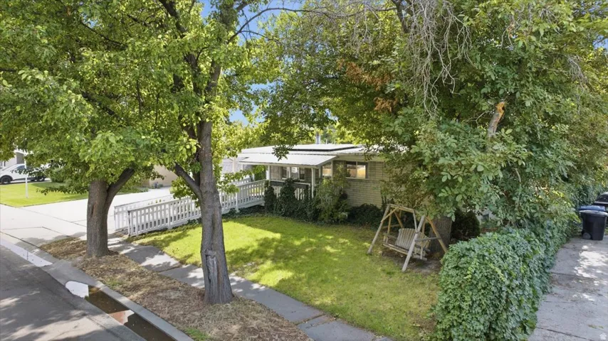 Manicured front lawn with mature trees, a white picket fence, and a covered porch