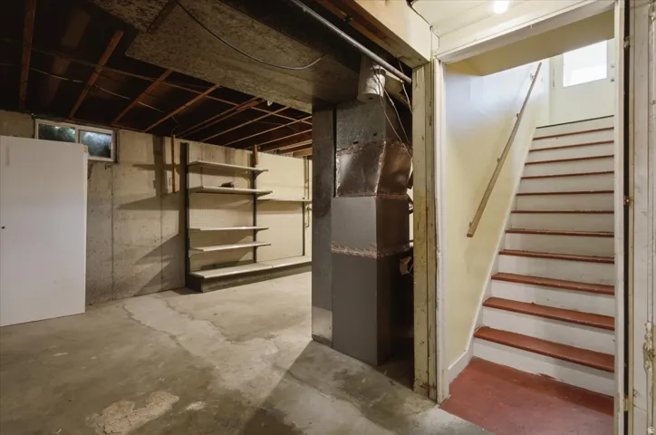 Concrete flooring, exposed ceiling joists, built-in shelving, basement window, and interior staircase with handrail