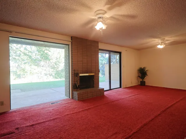 Living area featuring a brick fireplace, red carpet, and two ceiling fans