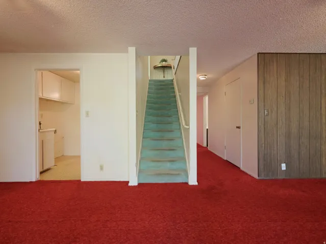 Red carpeted flooring, wood-paneled wall, interior staircase with carpeted treads, upper built-in shelving, and a built-in lower cabinet