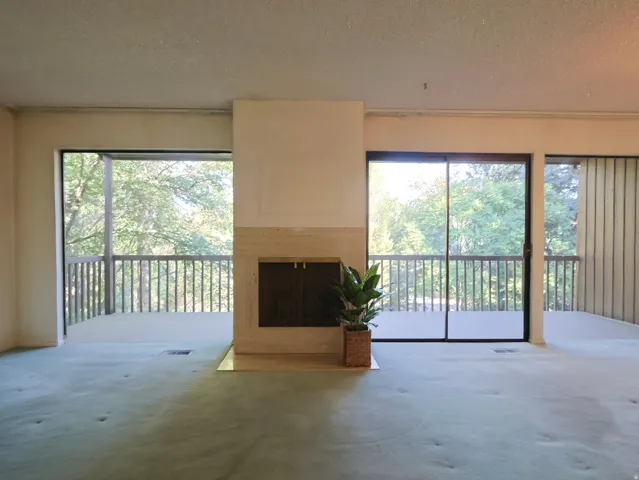 Fireplace with stone surround, two sliding glass doors, balcony access, and carpeted flooring