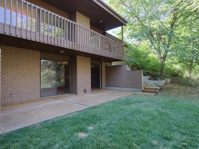 Brick exterior with a second-story balcony, multiple sliding glass doors, a concrete patio, and a grass lawn