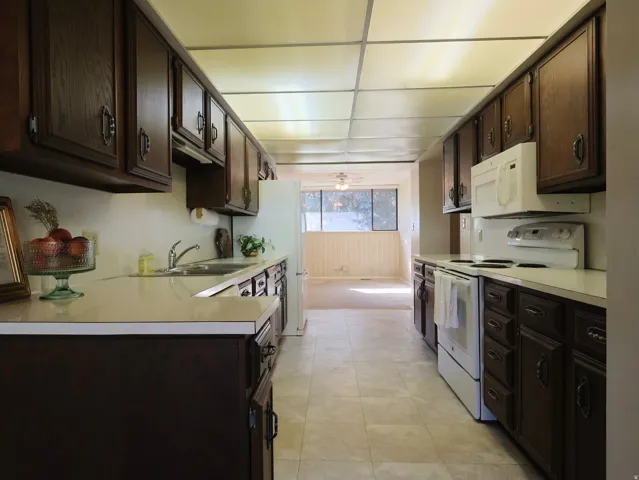 Galley kitchen featuring wood cabinetry, white countertops, tile flooring, and white appliances