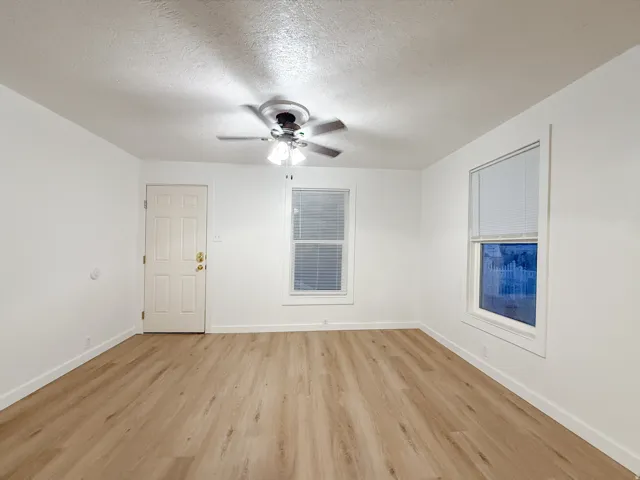 Wood-finish flooring, white painted walls, and a ceiling fan with integrated lighting