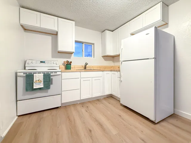 White shaker-style cabinetry, wood-finish countertops, stainless steel sink, built-in white range, and wood-finish flooring