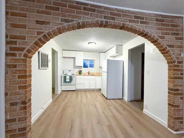 Brick archway with white walls, wood-finish flooring, white cabinetry, and white appliances