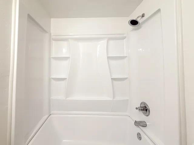 White tub and shower combination with chrome fixtures and integrated shelving