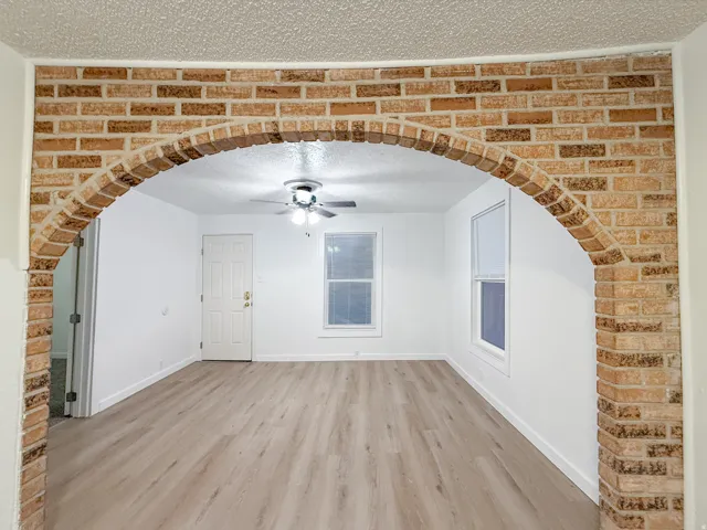 Brick archway entry framing a room with wood-finish flooring, white walls, and a ceiling fan with integrated lighting