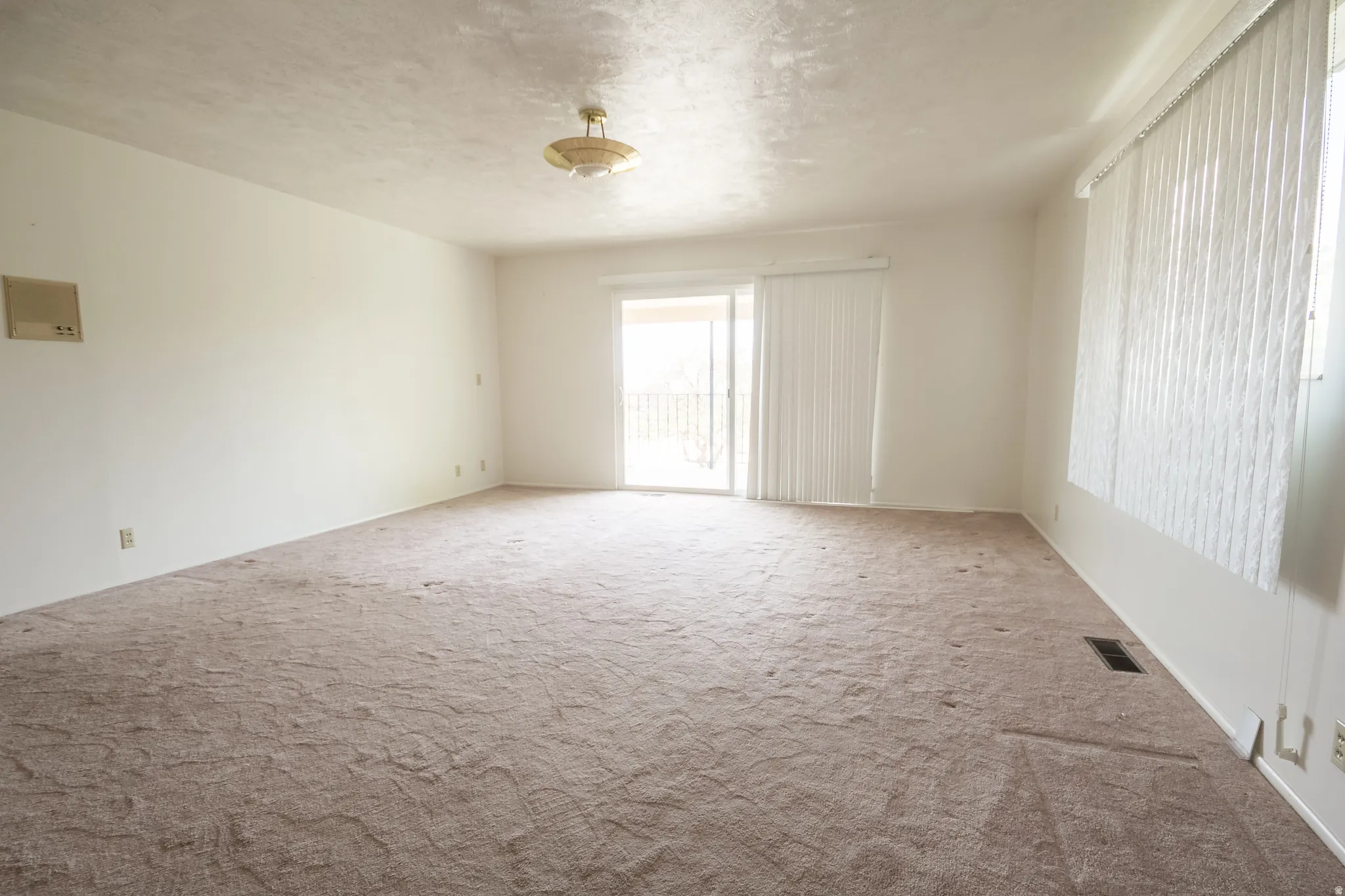 Sliding glass door leading to a balcony, ceiling-mounted light fixture, and vertical window blinds