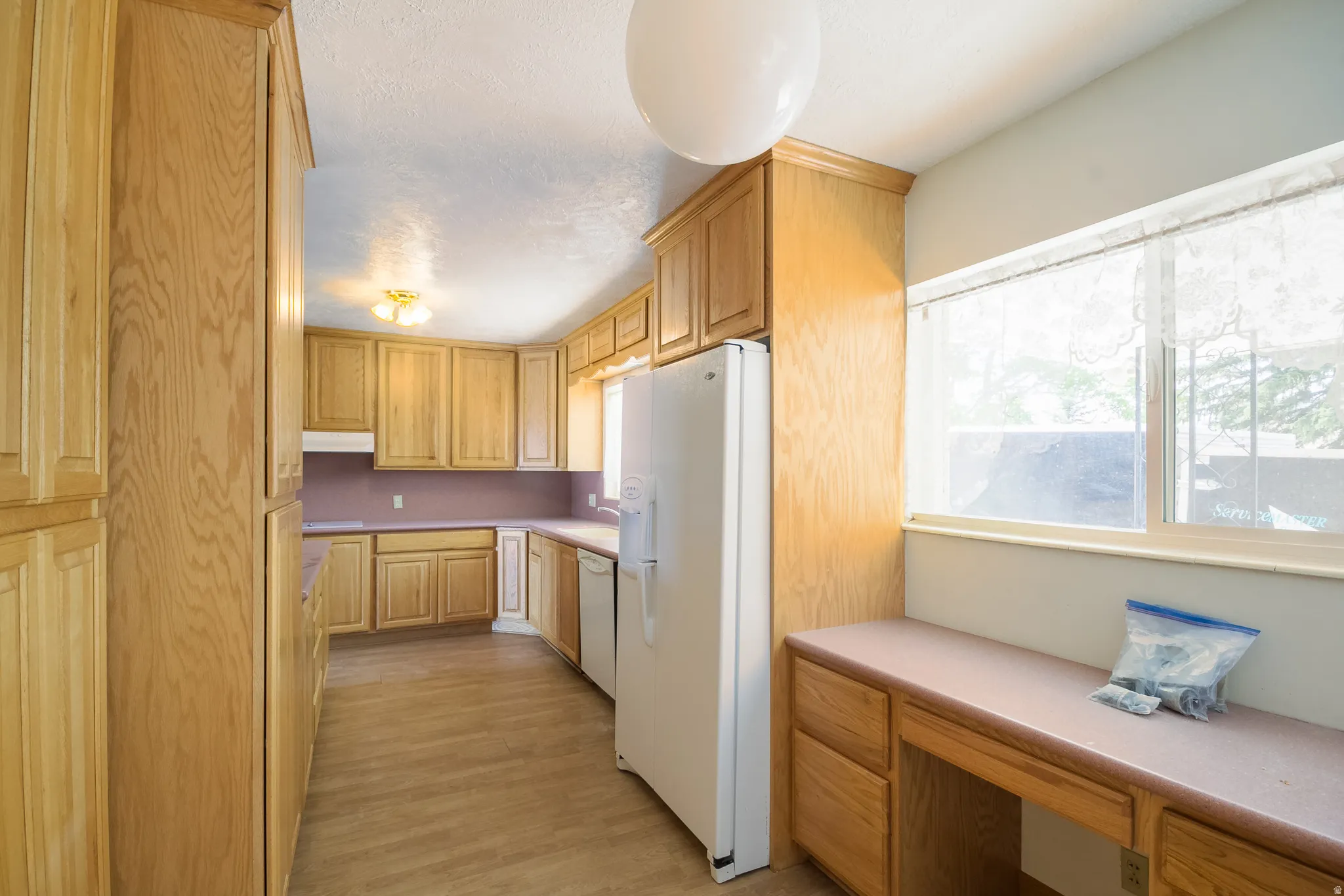 Kitchen featuring extensive wood cabinetry, laminate countertops, wood-finish flooring, a built-in desk area, and an integrated ceiling light fixture