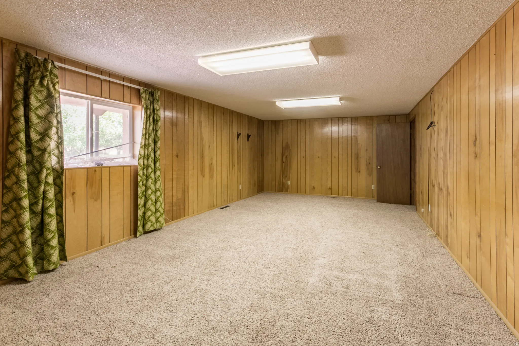 Spacious room featuring wood paneling, a single window, and neutral carpeting