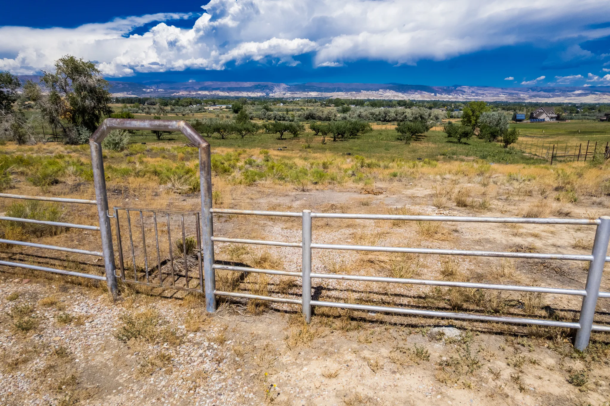 Expansive land parcel featuring a metal pipe fence, a metal gate, and distant mountain scenery