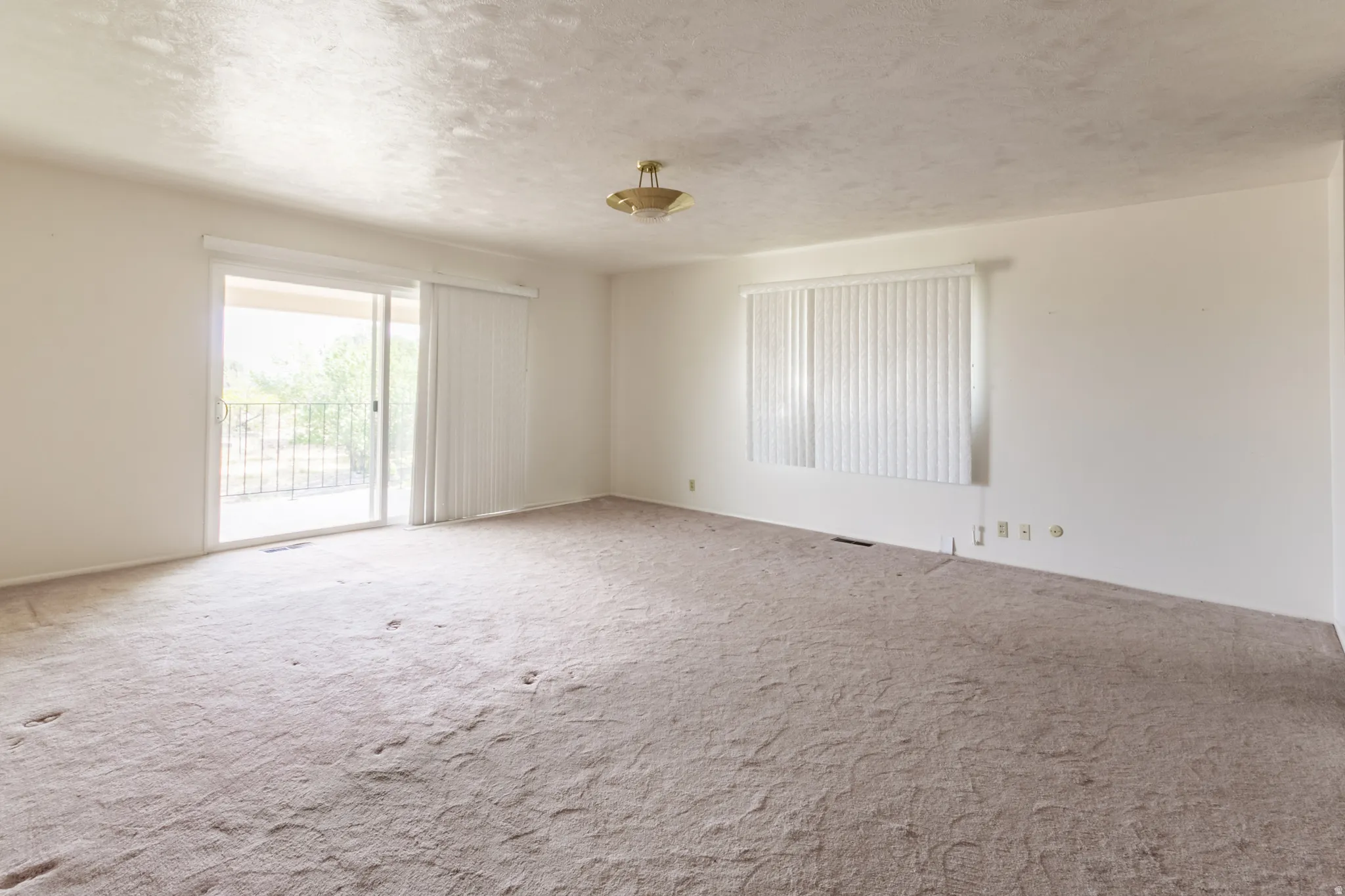 Sliding glass door leading to a balcony with an iron railing, single window with vertical blinds, and a flush mount light fixture