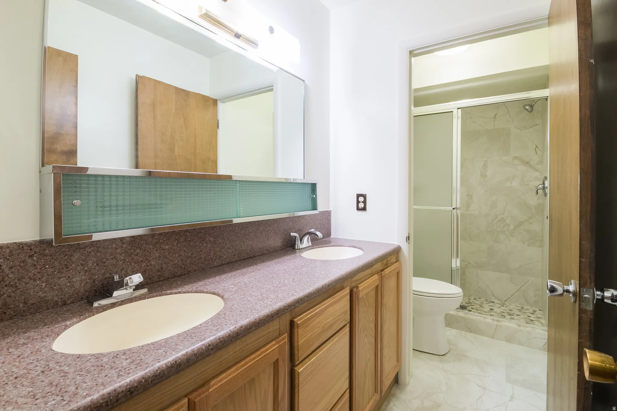 Dual basin vanity with a speckled countertop, integrated sinks, and wood-finish cabinetry