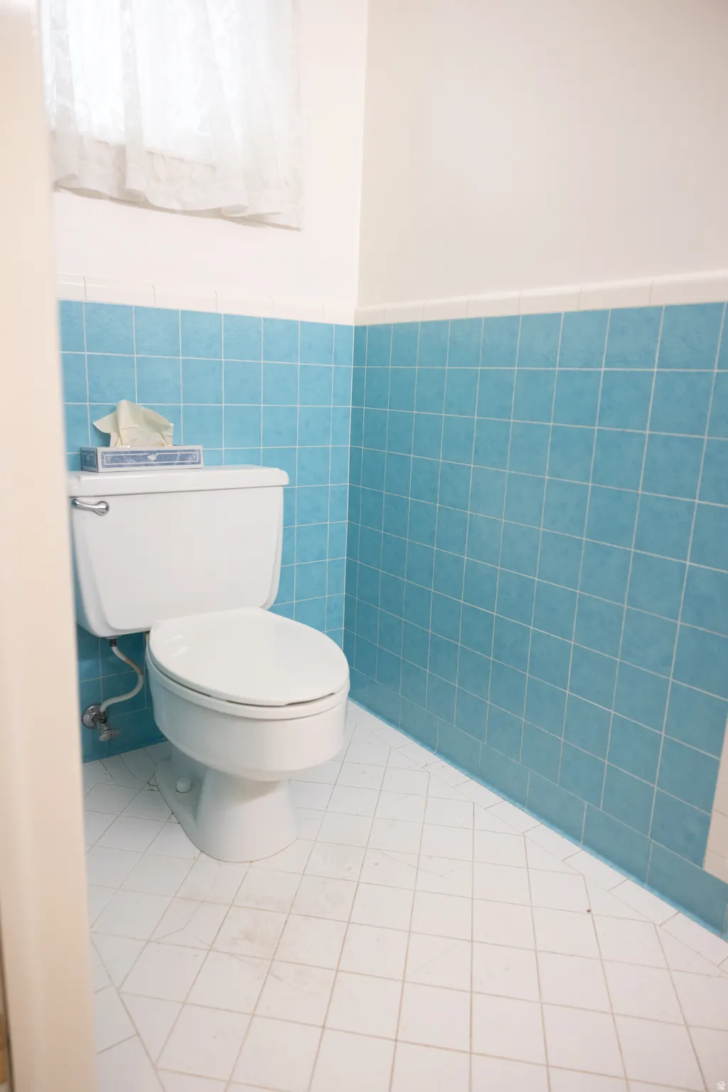 White toilet with a round bowl, blue square wall tiles, and white square floor tiles