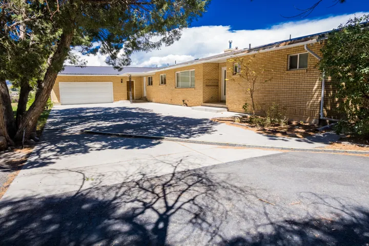 Brick exterior with a metal roof, an attached garage, a paved driveway, and mature landscaping