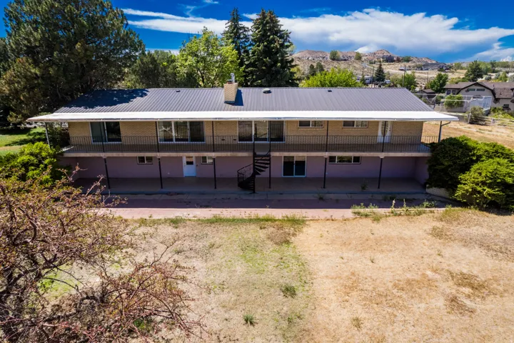 Two-story residence featuring a metal roof, an upper balcony with black railings, and a spiral staircase