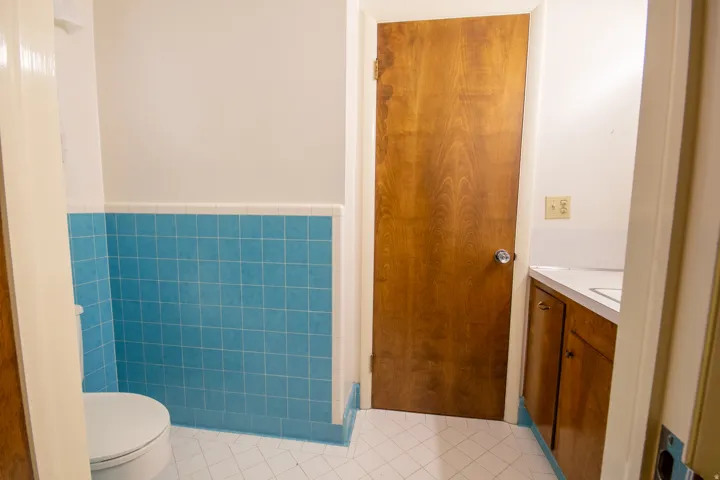 White tile flooring with blue grout, blue tiled wainscoting, and a wood-finish door
