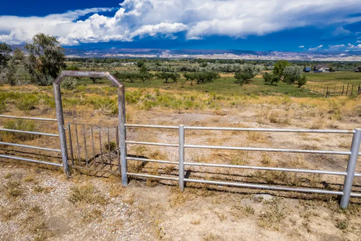 Expansive land parcel featuring a metal pipe fence, a metal gate, and distant mountain scenery