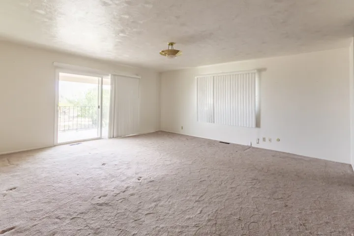 Sliding glass door leading to a balcony with an iron railing, single window with vertical blinds, and a flush mount light fixture