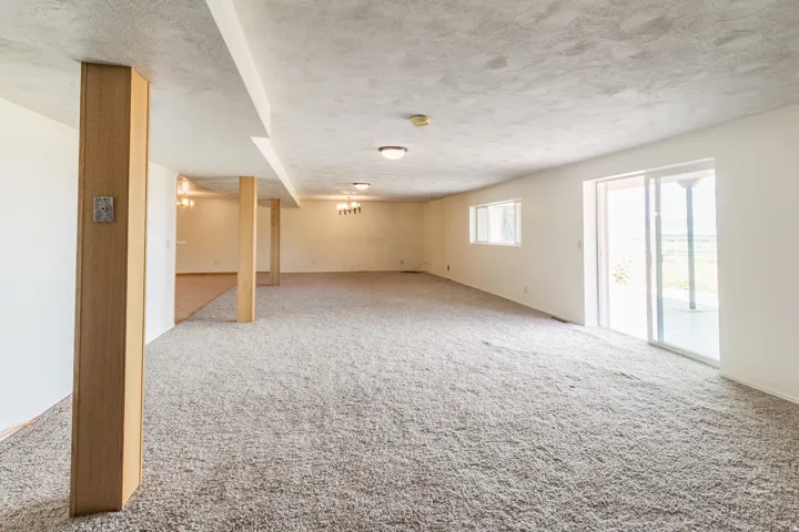 Expansive carpeted area with recessed lighting, exposed wood-finish beams, and multiple windows