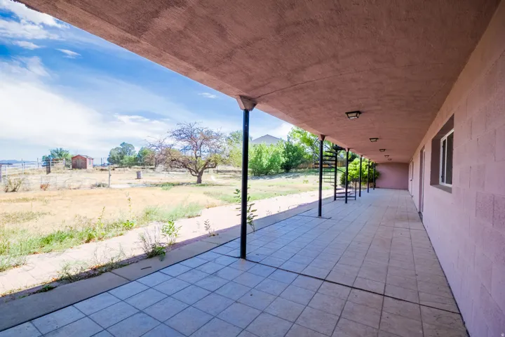 Extended covered patio with tile flooring, featuring multiple support columns, a spiral staircase, exterior lighting fixtures, and a large open yard beyond