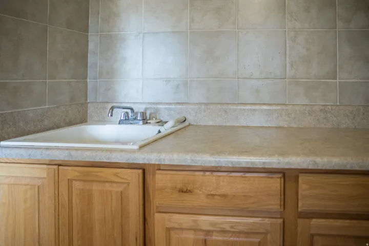 Utility sink with chrome-finish faucet, laminate countertop, ceramic tile backsplash, and wood-finish cabinetry