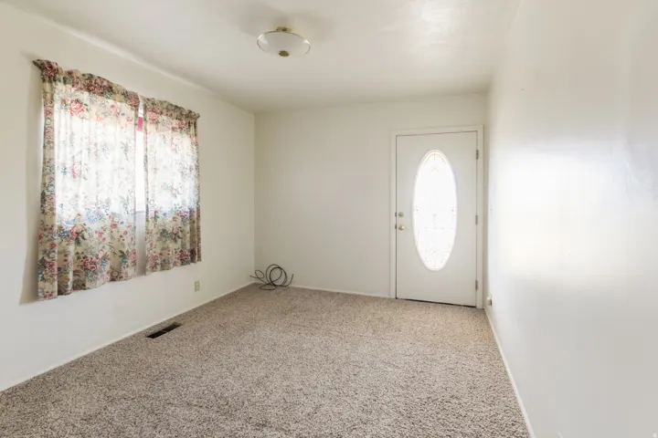White interior walls, neutral carpet flooring, ceiling-mounted light fixture, and an entry door with an oval-shaped glass insert