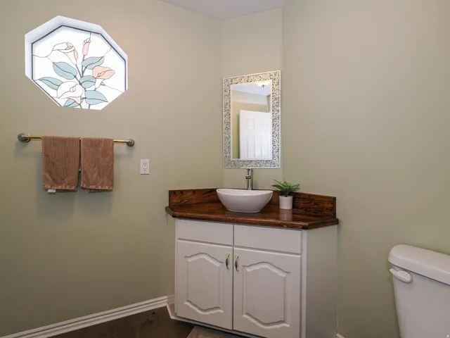 Elegant powder room featuring a custom wood-finish vanity with an integrated vessel sink, decorative mirror with brushed metal frame, and coordinating towel bar
