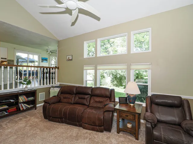 Vaulted ceiling with a ceiling fan, multiple windows with roller shades, and a half-wall partition with a wood cap