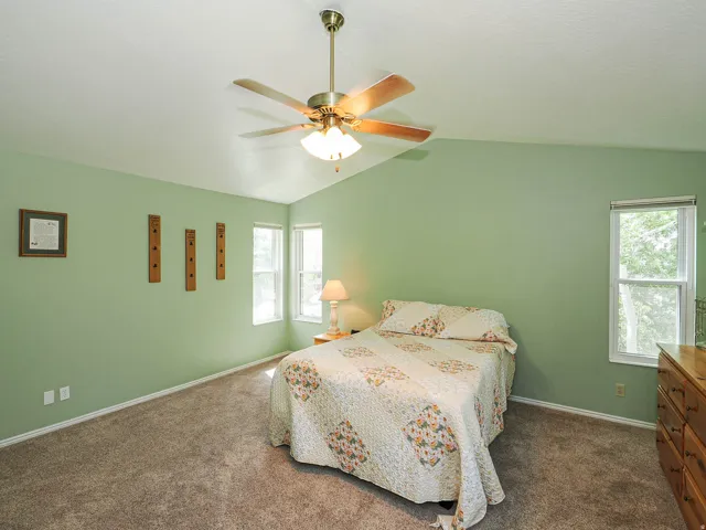 Vaulted ceiling with a brass-finish ceiling fan, multiple windows providing natural light, and plush carpeting