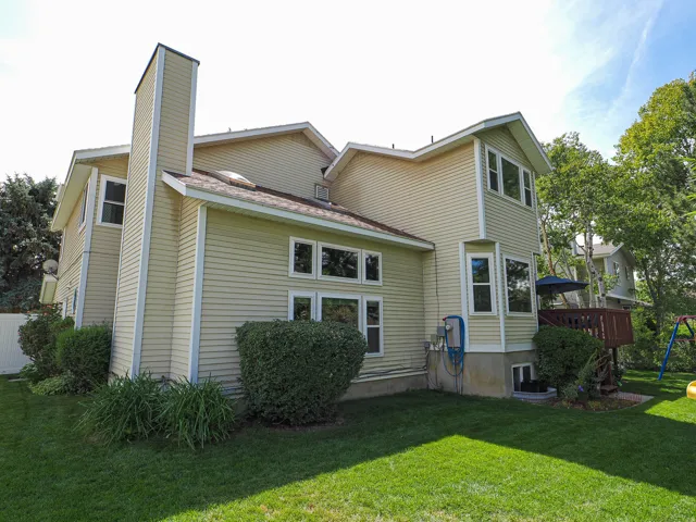 Exterior featuring light-colored siding, a prominent chimney, multiple windows, a rear deck, and a green lawn