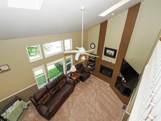 Vaulted ceiling with skylights, multiple windows, brick fireplace, and ceiling fan