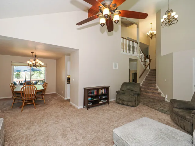 Vaulted ceiling with a ceiling fan, carpeted flooring, formal dining space, staircase with white balusters, and decorative chandeliers
