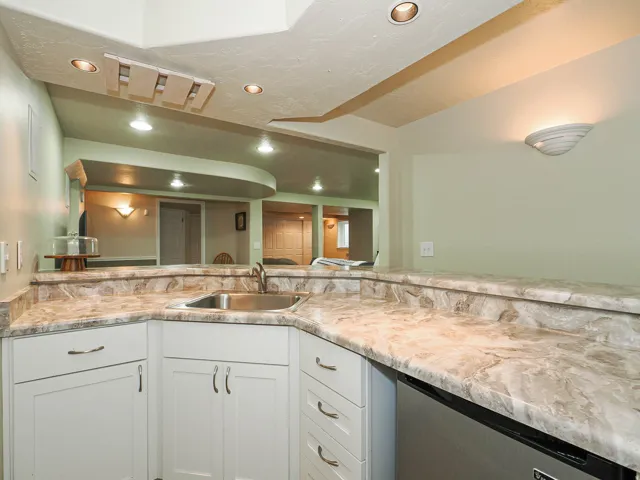 Built-in wet bar featuring a stainless steel sink, white cabinetry with silver hardware, stone-look countertops, and recessed lighting