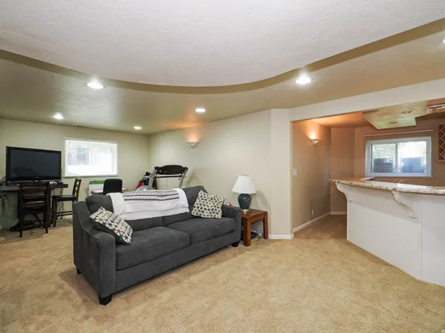 Recessed lighting, wall sconces, ceiling with a decorative curved soffit, carpeted flooring, and a built-in counter with a stone-finish surface