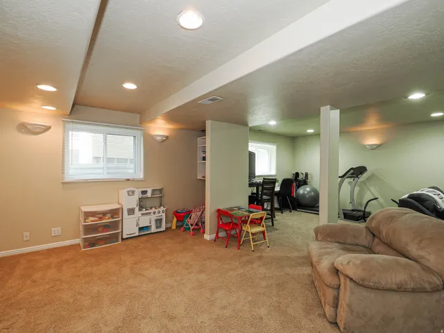 Carpeted recreation area with recessed lighting, wall sconces, and natural light from a window