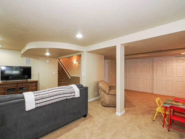 Recessed ceiling lighting, wall-to-wall carpeting, wood-finish media console, built-in storage closets, and an interior staircase with wood railing