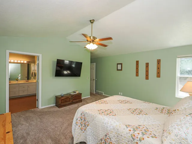 Carpeted room with a ceiling fan, wall-mounted television, and a window